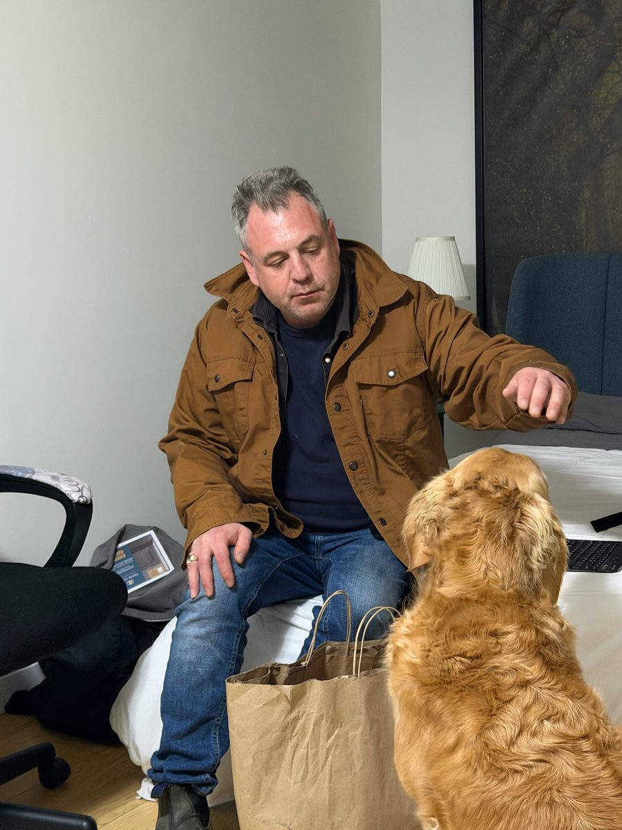 Anthony McGrath Tooton IV in a brown jacket, reaching out to a golden retriever