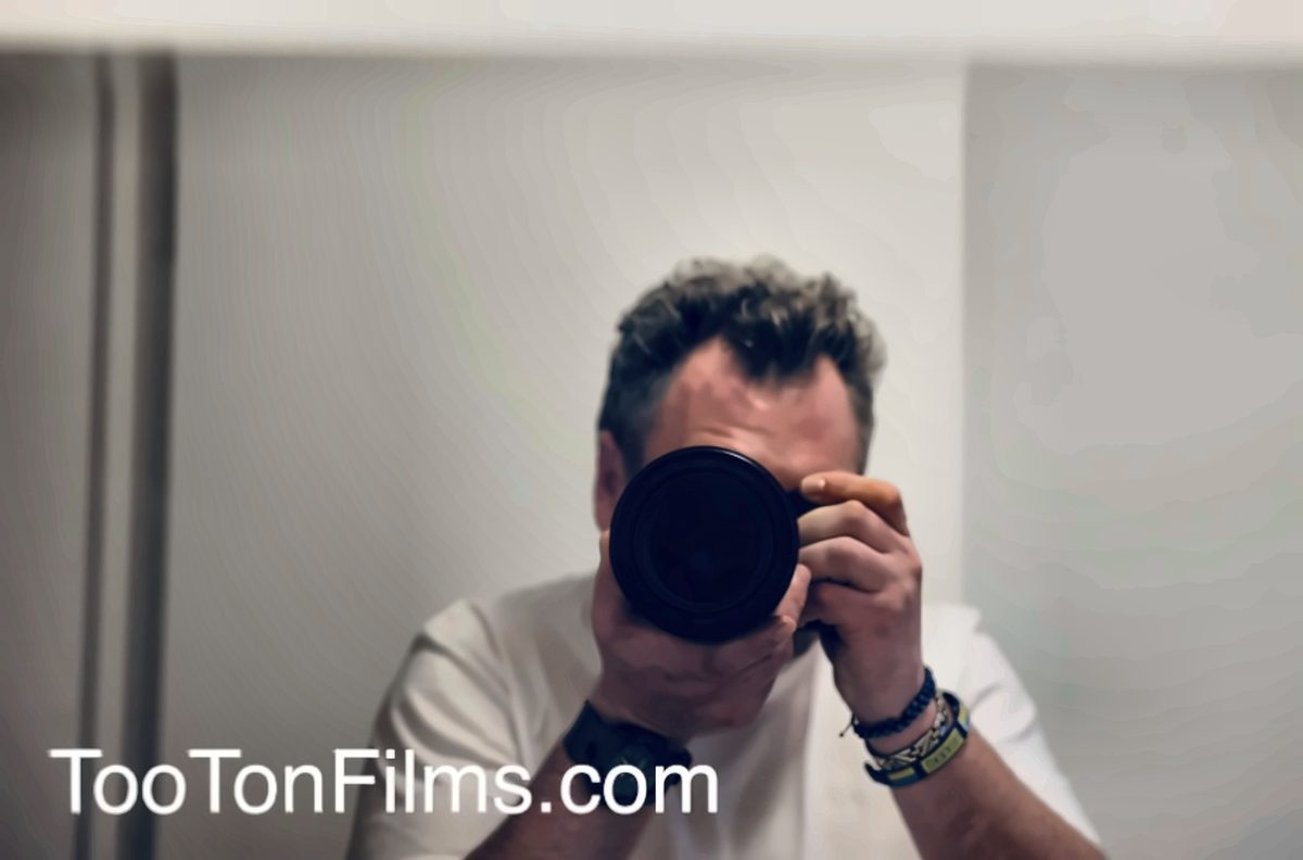 Anthony McGrath Tooton IV photographing his reflection in a mirror, camera raised to his face